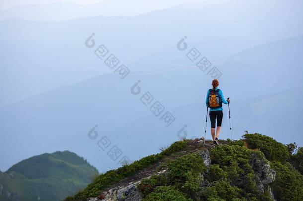在悬崖边上有追踪棍和后袋的旅游女孩。风景与高山。无尽无垠的地平线上。温暖阳光明媚的夏日.