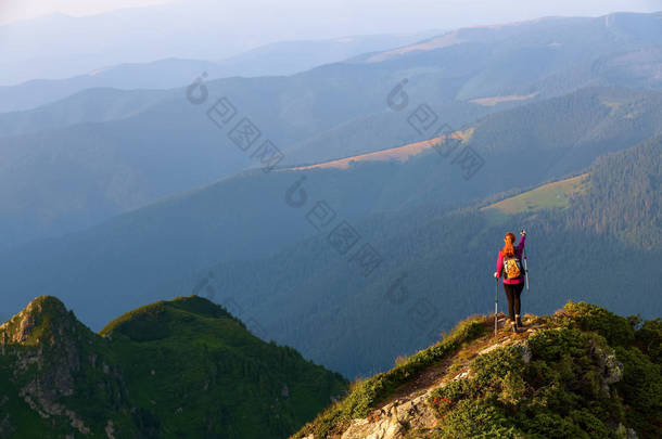 在高山和田野的风景中, 草坪上的深渊边缘有一个带着背包和徒步手杖的游客, 并指明了道路.