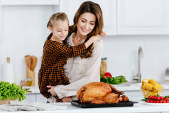 美丽的年轻母亲和女儿拥抱, 同时烹饪感恩节火鸡一起
