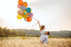 爱夫妇与气球拥抱在黑麦领域。夏日草地上的美女