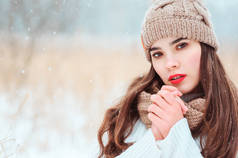 冬季特写美丽的年轻女子在针织帽子和毛衣走在户外 smowfall 下的肖像。红色口红的女孩变得温暖