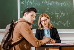 女教师看着年轻的学生在教室与黑板的背景