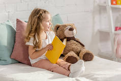 可爱的孩子玩泰迪熊和阅读书籍在床上的儿童房