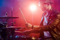 年轻的男性音乐家在舞台上的摇滚音乐会打鼓皮夹克的侧视图