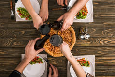 在木桌上吃比萨饼和沙拉的时候, 朋友们在一起敬酒的裁剪视图