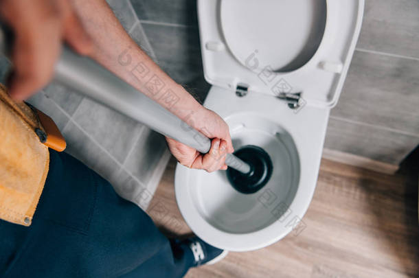 使用柱塞和清洁厕所在浴室的男性水管工裁剪拍摄