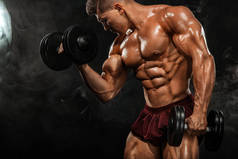 残酷强壮的肌肉健美运动的人在黑色背景上, 用哑铃抽打肌肉。锻炼健美的概念。体育营养广告的复制空间.