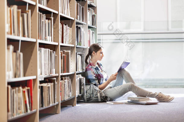 学生在图书馆坐在书架上看书
