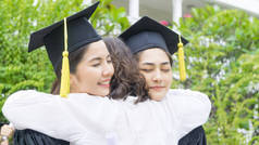 两名亚裔女学生带着毕业礼服和帽子拥抱父母在祝贺仪式.