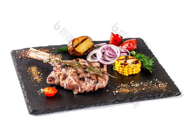 大肉牛排在骨头上，烤，与烤蔬菜，玉米，红洋葱，甜辣椒，土豆一起食用。餐厅里用黑板擦上的现代餐具.
