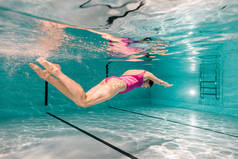woman diving underwater in pink swimwear in swimming pool