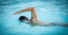 男子游泳者在蓝色的游泳池里爬泳.一名身穿泳镜的年轻男子游泳爬行运动员的肖像。铁人三项全能运动员训练.