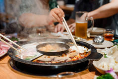 人们在中餐馆吃火锅晚餐。用筷子吃饭, 用煮汤煮生的食物块.