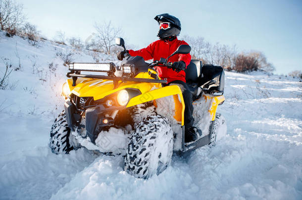 身穿红色保暖冬衣和黑色头盔的年轻男子司机在大雪中与深轮轨道的 atv 4wd 四轮自行车站。摩托冬季运动.