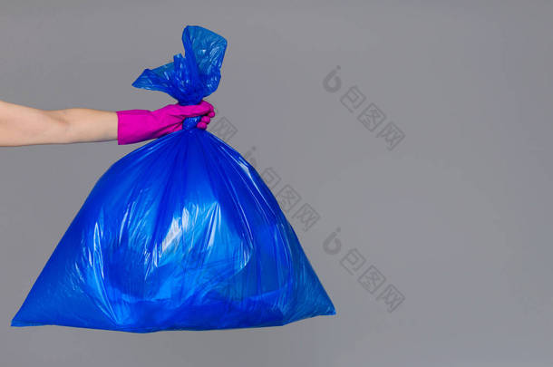 一个女人的手拿着一个装满垃圾的蓝色塑料袋.
