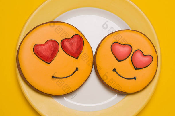 两个黄色的饼干, 呈微笑的形状, 眼睛呈心脏形状, 躺在盘子里, 在黄色的背景上, 有约会和爱情的概念