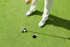 在阳光明媚的日子里, 活跃的男子拿着高尔夫球杆, 同时要把它打到绿地的洞里