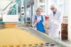 在现代食品厂，两个女人站在传送带上讨论生产的肖像，复制空间