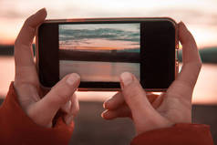 妇女手拿着手机, 照片上有山湖风景.