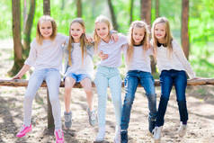 一群五个友好的女孩坐在树梁上, 在夏日森林里散步。明亮的阳光明媚的日子.