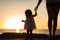 小女孩和她的母亲在海滩上看日落。剪影.