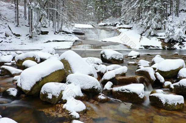 冬天在山区河流。流中的大石头满了新鲜的粉雪和懒水水平较低。森林中水位的思考.