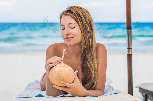年轻女子在沙滩上的<strong>贵妃</strong>椅上喝椰子牛奶.