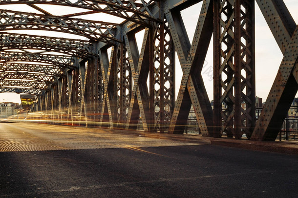 在一个阳光明媚的日子里, 沥青路在一座城市桥的<strong>钢结构</strong>下。<strong>桥梁</strong>隧道中的城市场景。长时间曝光。色调