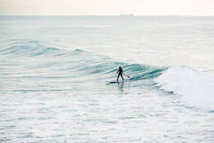 冲浪者在蓝色波浪上站立桨板。海洋冬季冲浪