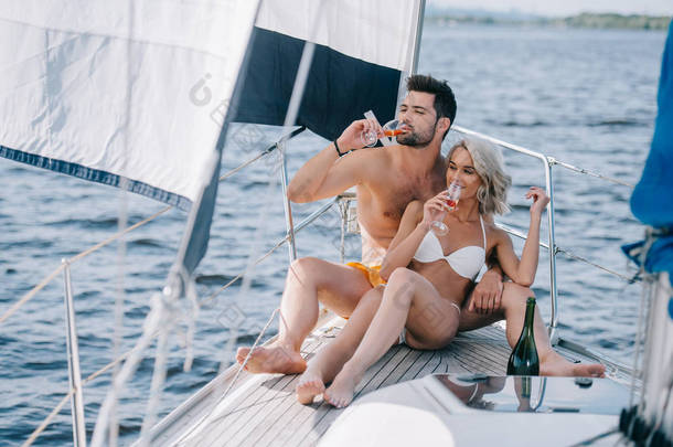 微笑的情侣在泳装喝香槟在游艇上