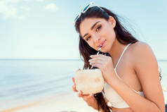 美丽的女孩比基尼在海滩上喝椰子鸡尾酒