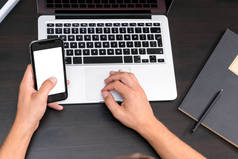 在老式木桌上使用笔记本电脑时, 曼斯手在智能手机上打字。在键盘上键入指针。顶级视野, 商务办公场所