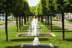 小巷里的街边喷泉。城市里的夏天炎热的一天。交通街道之间有绿树和绿草。小喷泉