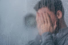 在窗口与人覆盖的面孔和哭泣在背景上的雨滴的选择性焦点