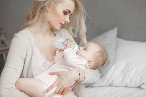 年轻的母亲喂她可爱的小女儿与一瓶儿童配方<strong>奶粉</strong>。妇女与她的新生儿在家。妈妈照顾一个孩子。母乳喂养的替代方法.