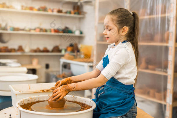 美丽的小女孩在陶艺作坊做一壶黏土