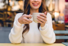 愉快的女孩拿着杯子与咖啡在咖啡馆的裁剪视图