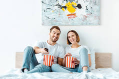 快乐微笑的夫妇在床上吃爆米花和看电视