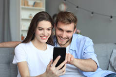 一对年轻夫妇坐在客厅的沙发上，用智能手机观看网上内容.
