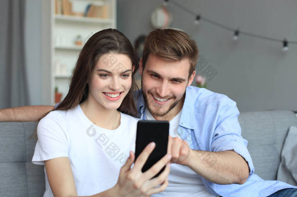一对年轻夫妇坐在客厅的沙发上，用智能<strong>手机</strong>观看网上<strong>内容</strong>.