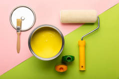 在粉红色和绿色表面上用黄色油漆、瓶子、刷子和油漆辊的锡顶视图