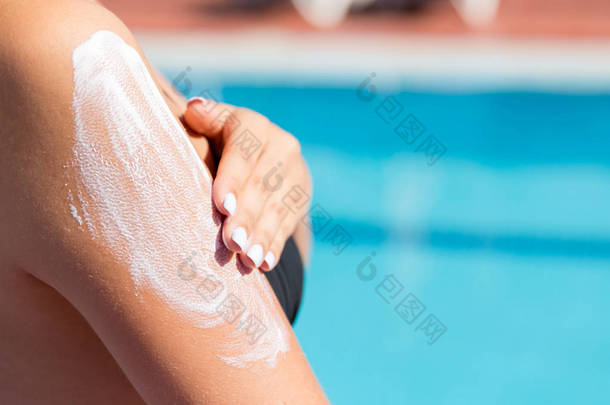 迷人的女孩戴着太阳帽,在游泳池边的肩上涂防晒霜.度假时的防晒系数，概念