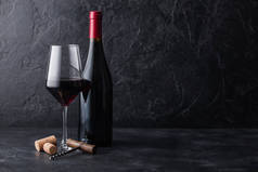 优雅的玻璃杯和一瓶红葡萄酒，黑色石头背景上有软木塞和软木塞。自然光