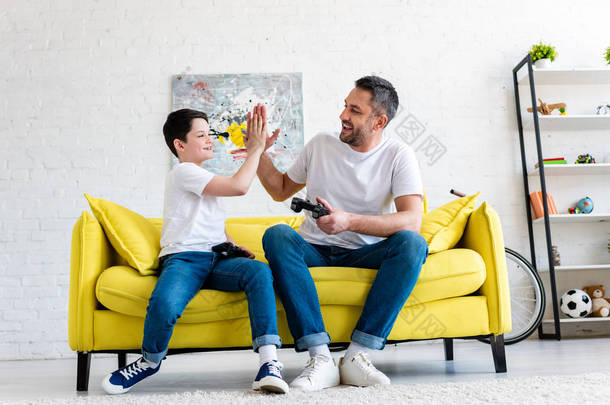 父亲和儿子做高五手势，而玩视频游戏在沙发上在家里