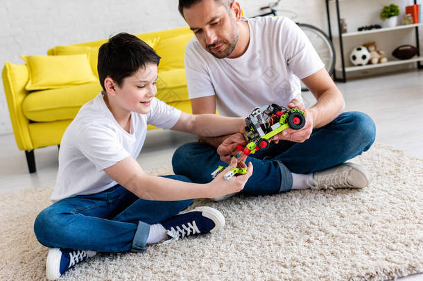 父亲和儿子坐在地毯上，在家里玩玩具车