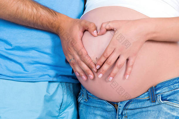 父母的爱和幸福的母性。怀孕肚子背景上心脏形状的特写