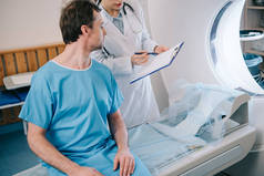 年轻放射科医生向坐在ct扫描仪床上的病人显示诊断的部分视图