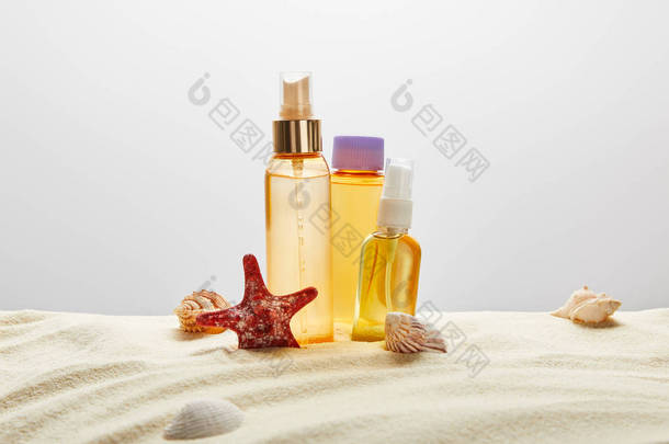 在灰色的背景上用贝壳和海星在沙中三个透明瓶子中晒太阳的产品