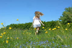 一个穿着白色连衣裙、头发飘逸的女孩穿过盛开的草地，背景.