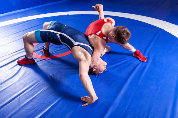 两名身着红色和蓝色制服的年轻运动员<strong>摔</strong>跤手<strong>摔</strong>跤，<strong>摔</strong>跤地毯，上面看.
